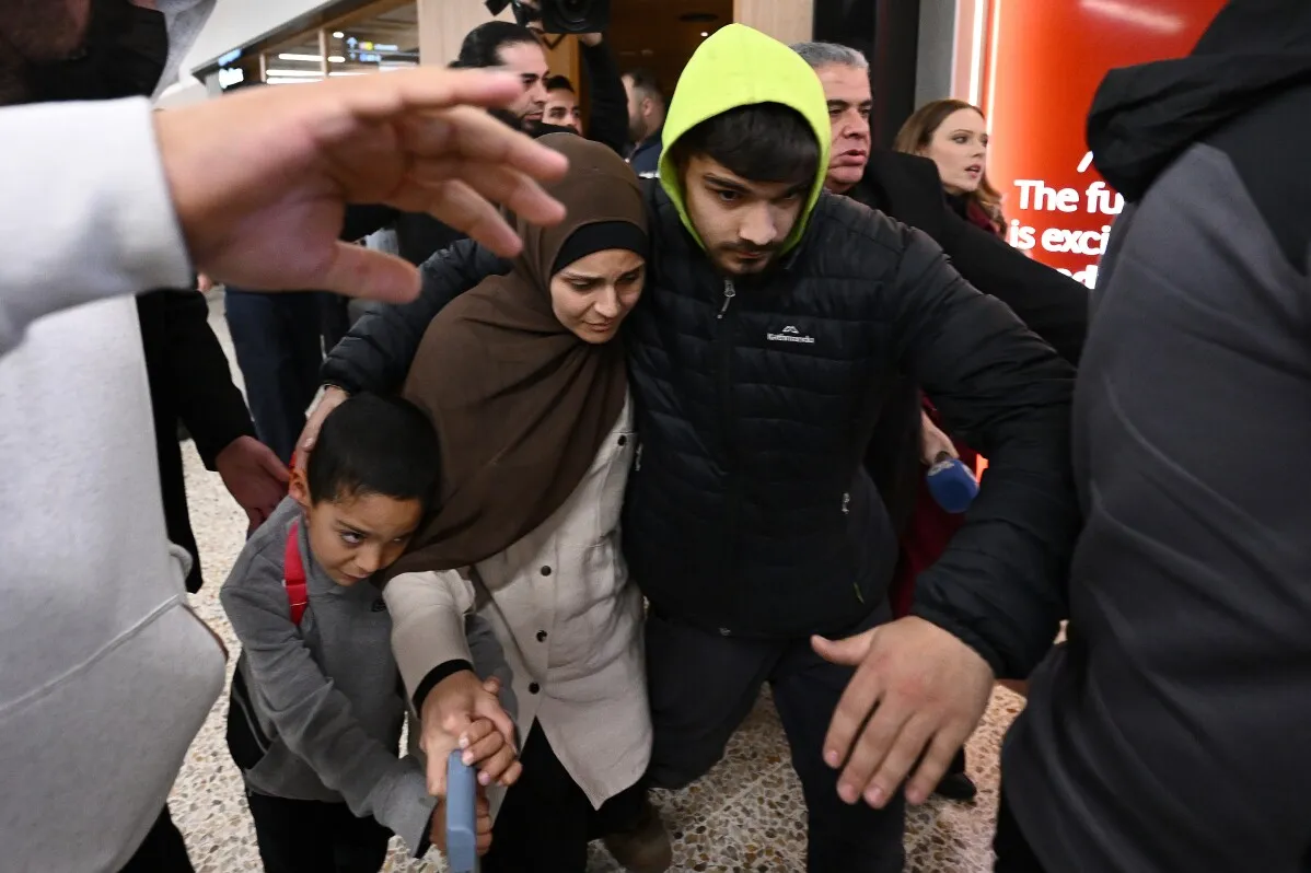 نساء وأطفال أستراليون يصلون إلى مطار بعد عودتهم من سوريا، وسط إجراءات أمنية، حيث يواجهون اتهامات بالإرهاب والاستعباد.