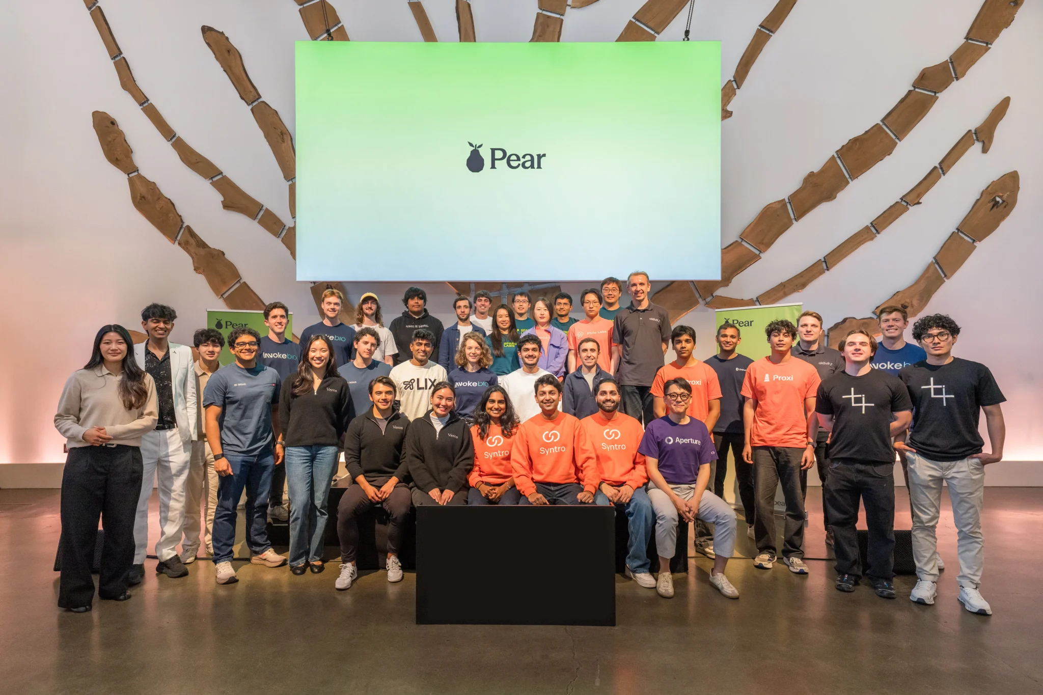 فرق الشركات الناشئة المشاركة في يوم عرض PearX في سان فرانسيسكو، مع شعار PearX في الخلفية، يعكس تنوع الابتكارات في الذكاء الاصطناعي والرقائق والروبوتات.