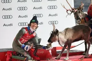 لوكاس بينهيرو براثن يحتفل بفوزه في كأس العالم للتزلج الألبي، بجانب حيوان الرنة، مع خلفية تحمل شعار أودي.
