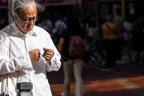 امرأة مسنّة ترتدي قميصًا أبيض وتربط خيطًا أحمر بعمود في حيّ Causeway Bay، تعبيرًا عن تعازيها لضحايا أحداث Tiananmen.