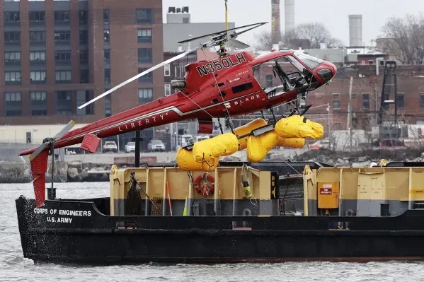 مروحية حمراء من طراز Liberty Helicopters تُرفع من نهر شرق نيويورك بواسطة سفينة تابعة للجيش، بعد حادث تحطم مأساوي.