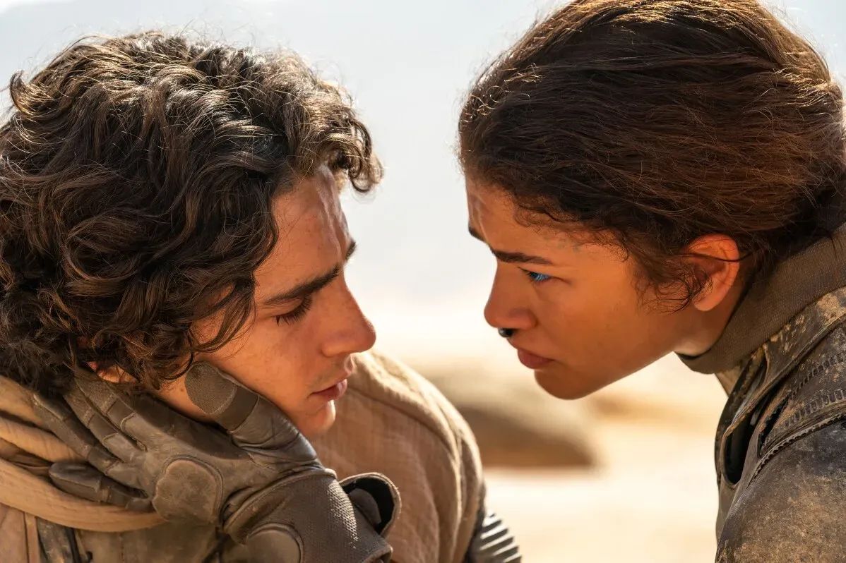 مشهد عاطفي من فيلم "Dune: الجزء الثاني" يظهر شخصيتين رئيسيتين تتواصلان في بيئة صحراوية، مما يعكس علاقتهما المعقدة.