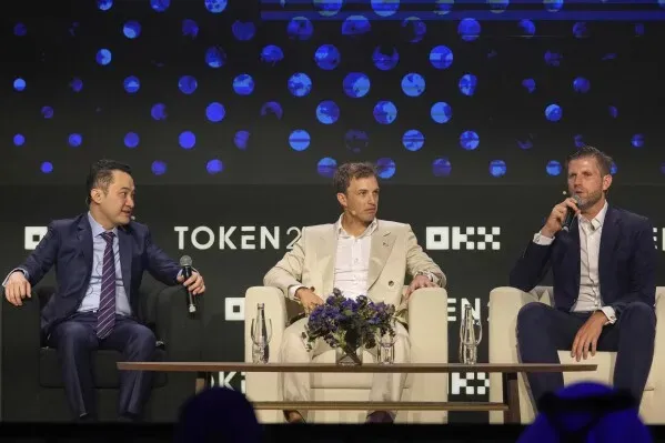 ثلاثة رجال يجلسون على منصة في حدث متعلق بالعملات الرقمية، يتحدثون عن مستقبل الصناعة وعلاقاتهم مع ترامب.