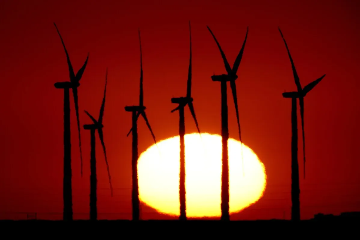تظهر توربينات الرياح silhouetted ضد شمس غاربة، مما يجسد التحول نحو الطاقة المتجددة والتعزيز البيئي في العالم.