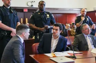 مرافعون ومحامون يجلسون في قاعة المحكمة بينما يراقبهم ضباط الشرطة، في سياق قضية لويجي مانجيوني.