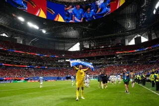 لاعب يحمل علمه بفخر في ملعب مليء بالجماهير، مع لافتات وأعلام تعكس روح كأس العالم والتنوع الثقافي.