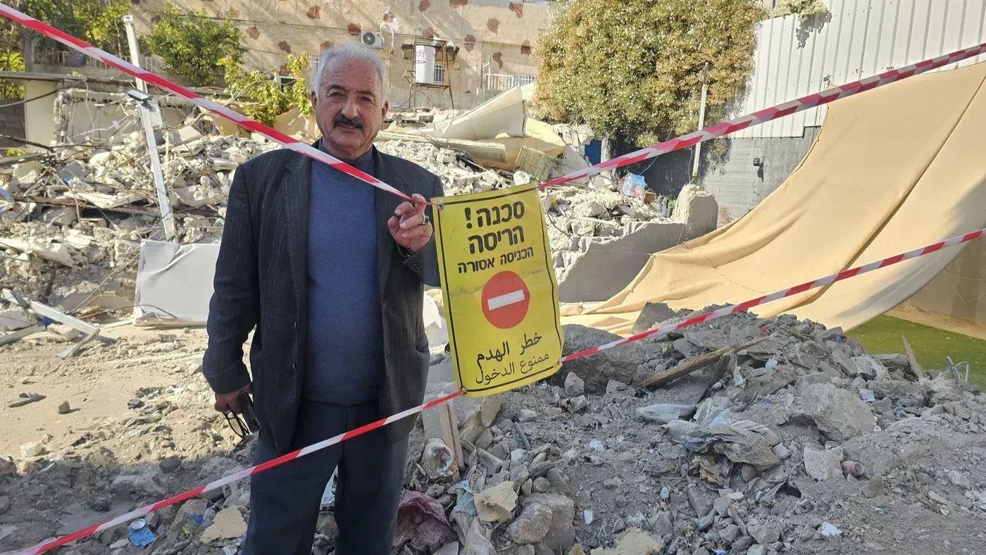 فخري أبو دياب يقف أمام أنقاض منزله المدمر في سلوان، مع لافتة تحذر من خطر الدخول، معبرًا عن شعور العجز بسبب التهجير.