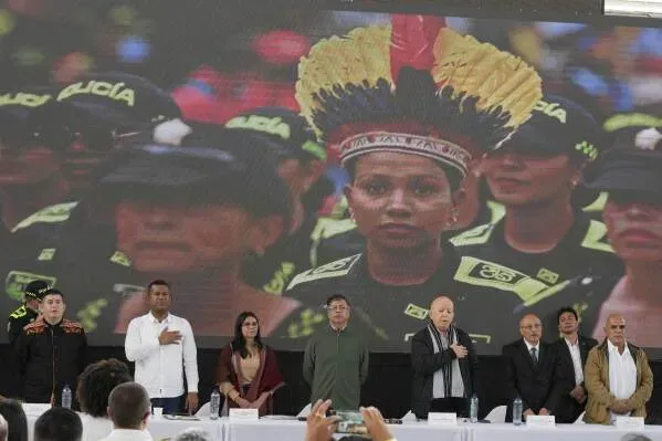 حفل تسليم الأسلحة في باستو، كولومبيا، حيث يقف مسؤولون حكوميون أمام شاشة تعرض صورة لامرأة ترتدي زياً تقليدياً.