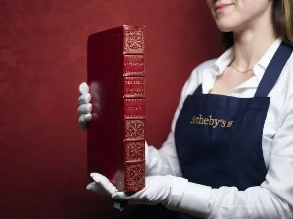نسخة نادرة من "أعمال ويليام شكسبير" تُعرض في مزاد، تُظهر غلاف الكتاب الأحمر اللامع مع تفاصيل دقيقة، تمسك بها موظفة من دار سوذبيز.