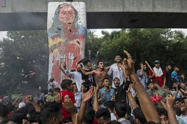 محتجون في دكا يحتفلون في تجمع حاشد، مع وجود جدارية ملونة خلفهم، تعبيرًا عن مطالبهم بالتغيير السياسي في بنغلاديش.