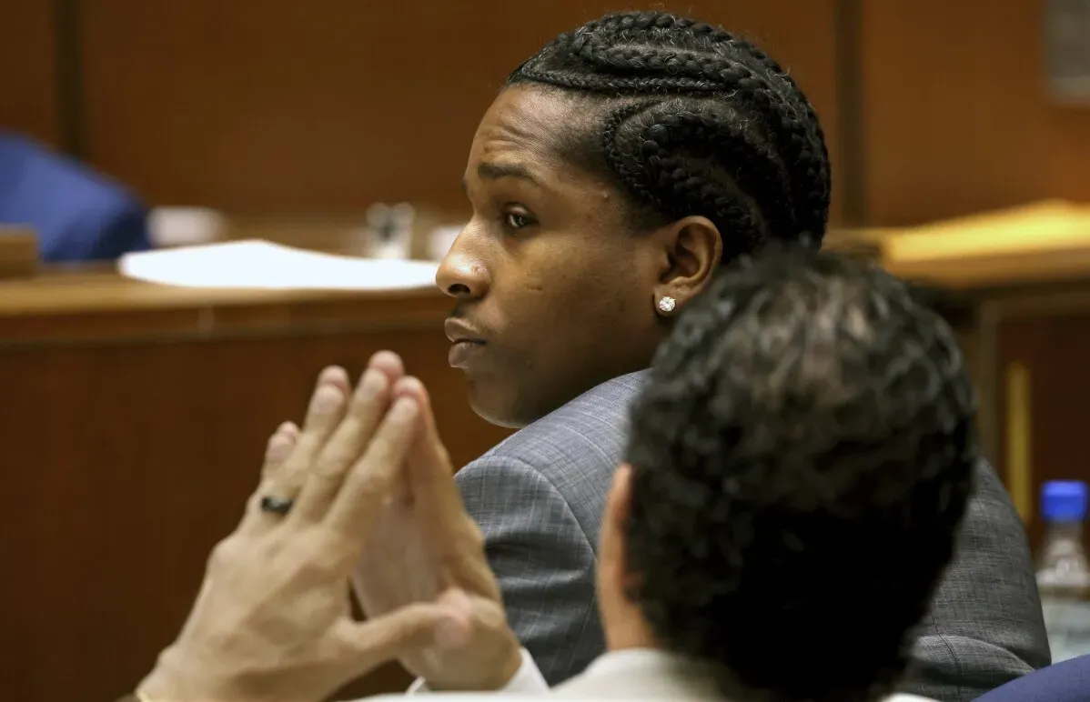 A$AP Rocky في قاعة المحكمة، يبدو مستمعًا بجدية أثناء جلسة شهادة تتعلق بقضية إطلاق نار مزعوم، مع تركيز على محاميه بجانبه.
