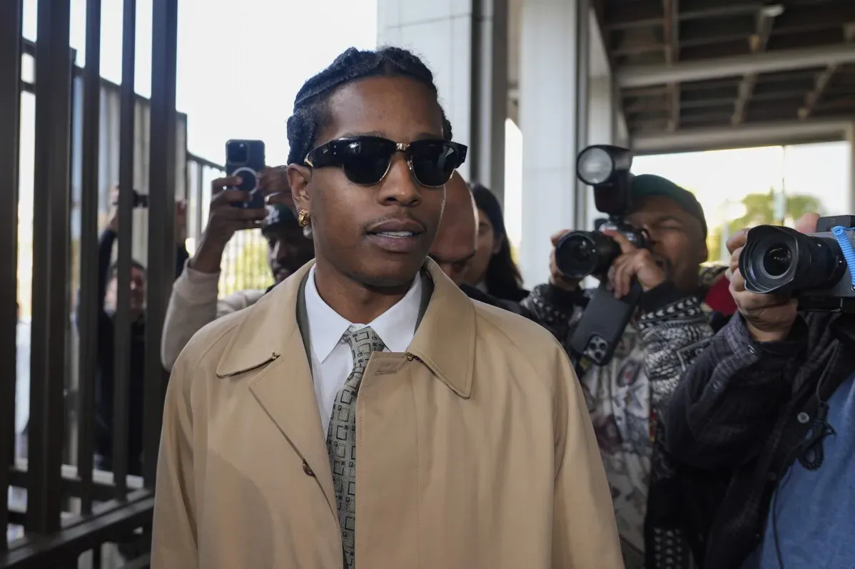 A$AP Rocky يغادر المحكمة محاطًا بالصحفيين، مرتديًا نظارات شمسية ومعطفًا بنيًا، وسط أجواء مشحونة خلال محاكمته بتهمة إطلاق النار.