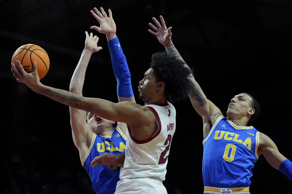 لاعب روتجرز يواجه لاعبي UCLA في مباراة كرة سلة، حيث يحاول تسجيل نقطة وسط ضغط الدفاع.