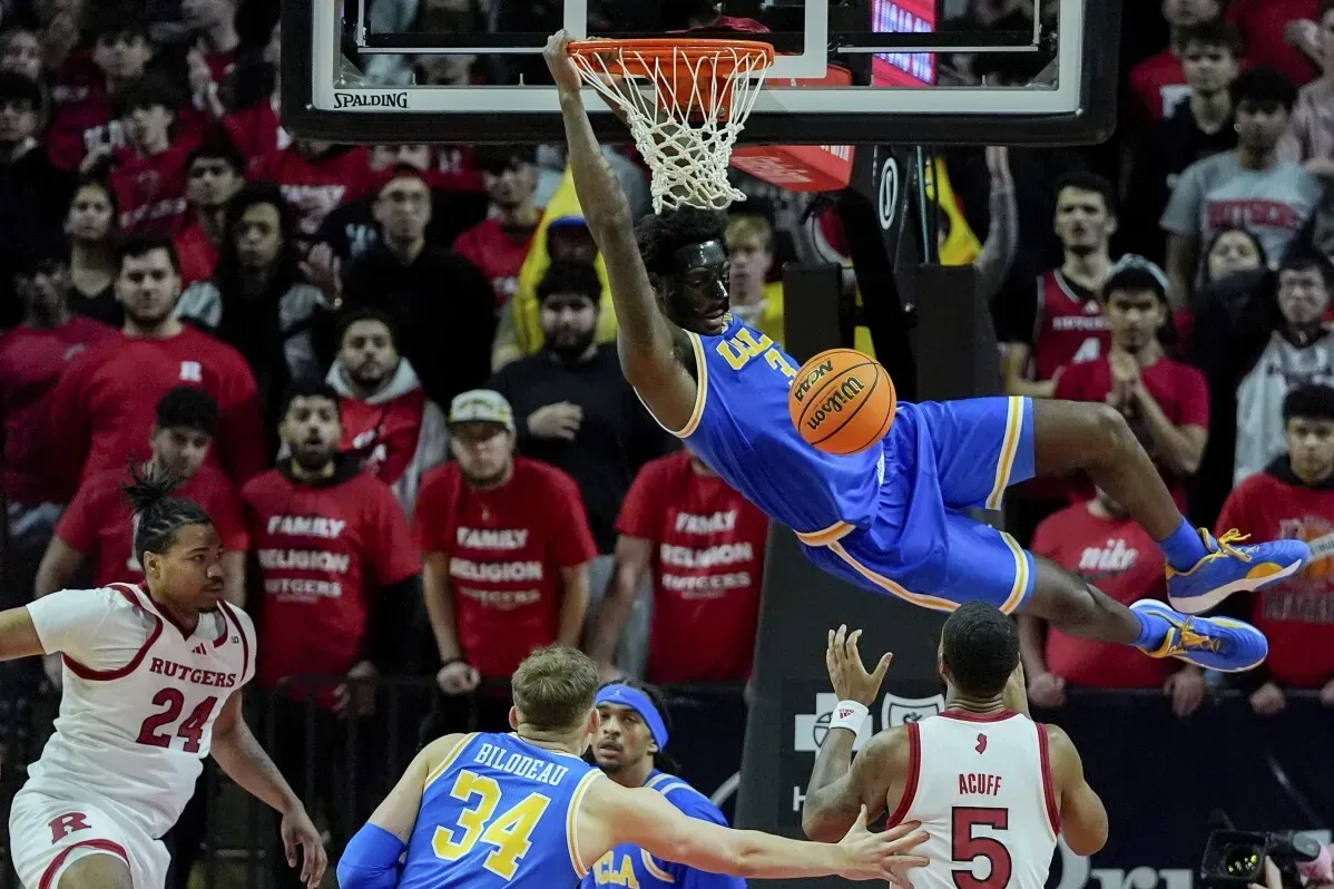 لاعب من فريق UCLA يقوم بسلة رائعة خلال مباراة ضد روتجرز، مع وجود مشجعين يرتدون قمصان حمراء في الخلفية.