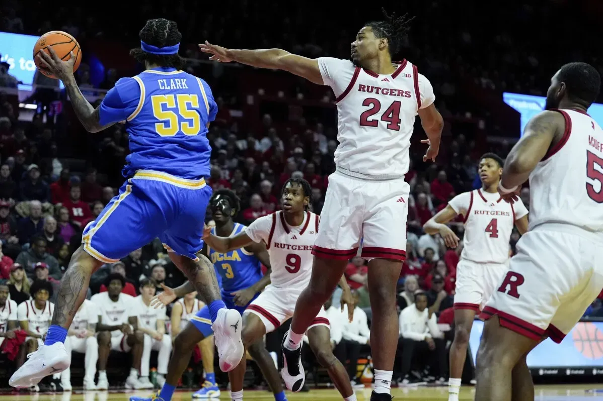 تظهر الصورة لاعب كرة سلة من فريق UCLA وهو يحاول التسجيل بينما يتصدى له لاعب من فريق روتجرز، وسط أجواء حماسية في الملعب.