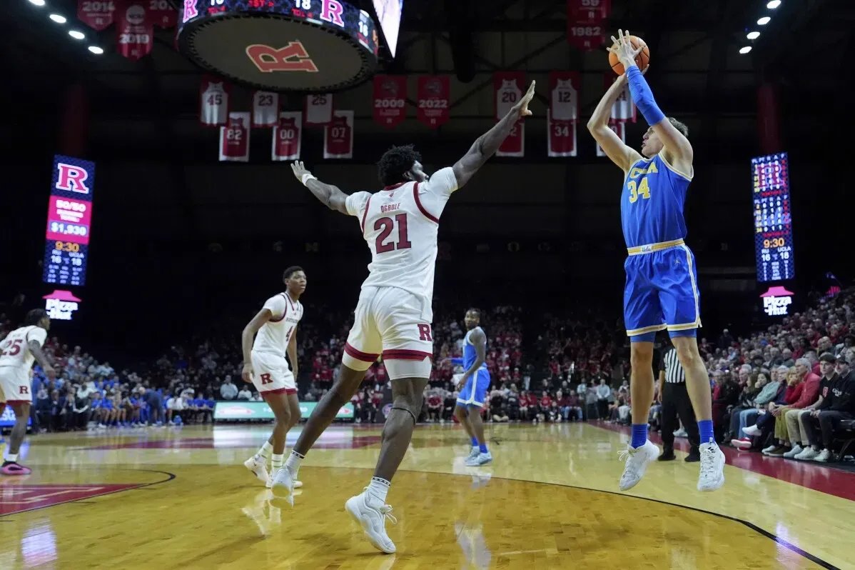 لاعب كرة سلة من فريق UCLA يسدد كرة بينما يحاول لاعب من روتجرز الدفاع عنه، في مباراة شهدت أداءً مميزًا من الفريقين.