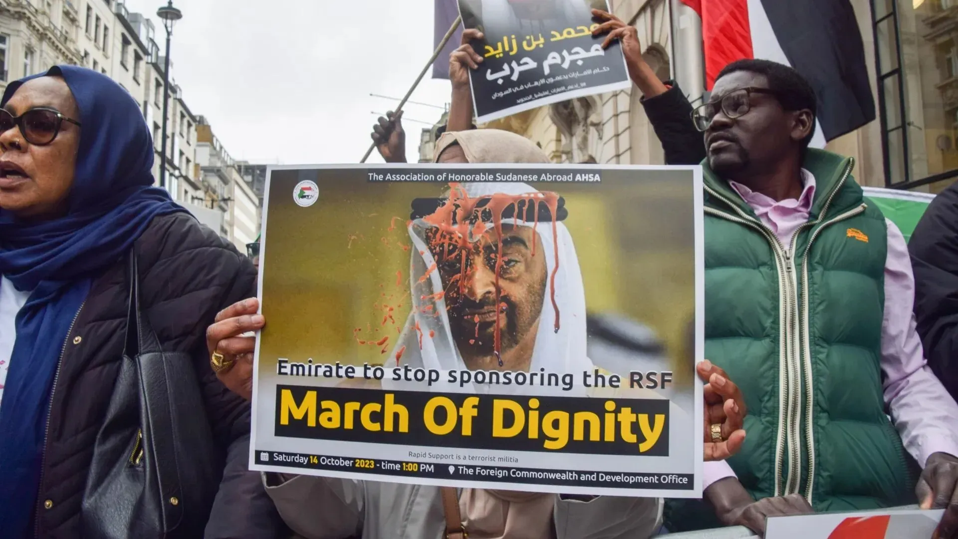 متظاهرون يحملون لافتة تطالب الإمارات بوقف دعم قوات الدعم السريع، مع صورة تبرز تأثير الحرب في السودان.
