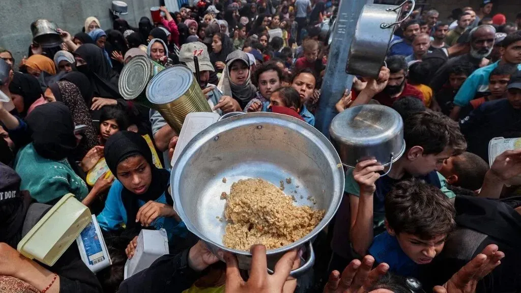 حشود من الناس يتزاحمون للحصول على المساعدات الغذائية في غزة، مع شخص يحمل وعاءً يحتوي على طعام، مما يعكس الحاجة الملحة للمساعدات الإنسانية.