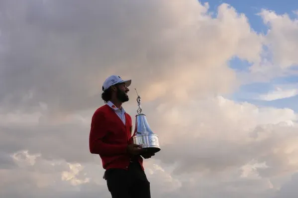 بهاتيا يحمل الكأس بعد فوزه ببطولة أرنولد بالمر إنفيتيشنال، مرتديًا سترة حمراء، مع سماء ملبدة بالغيوم في الخلفية.