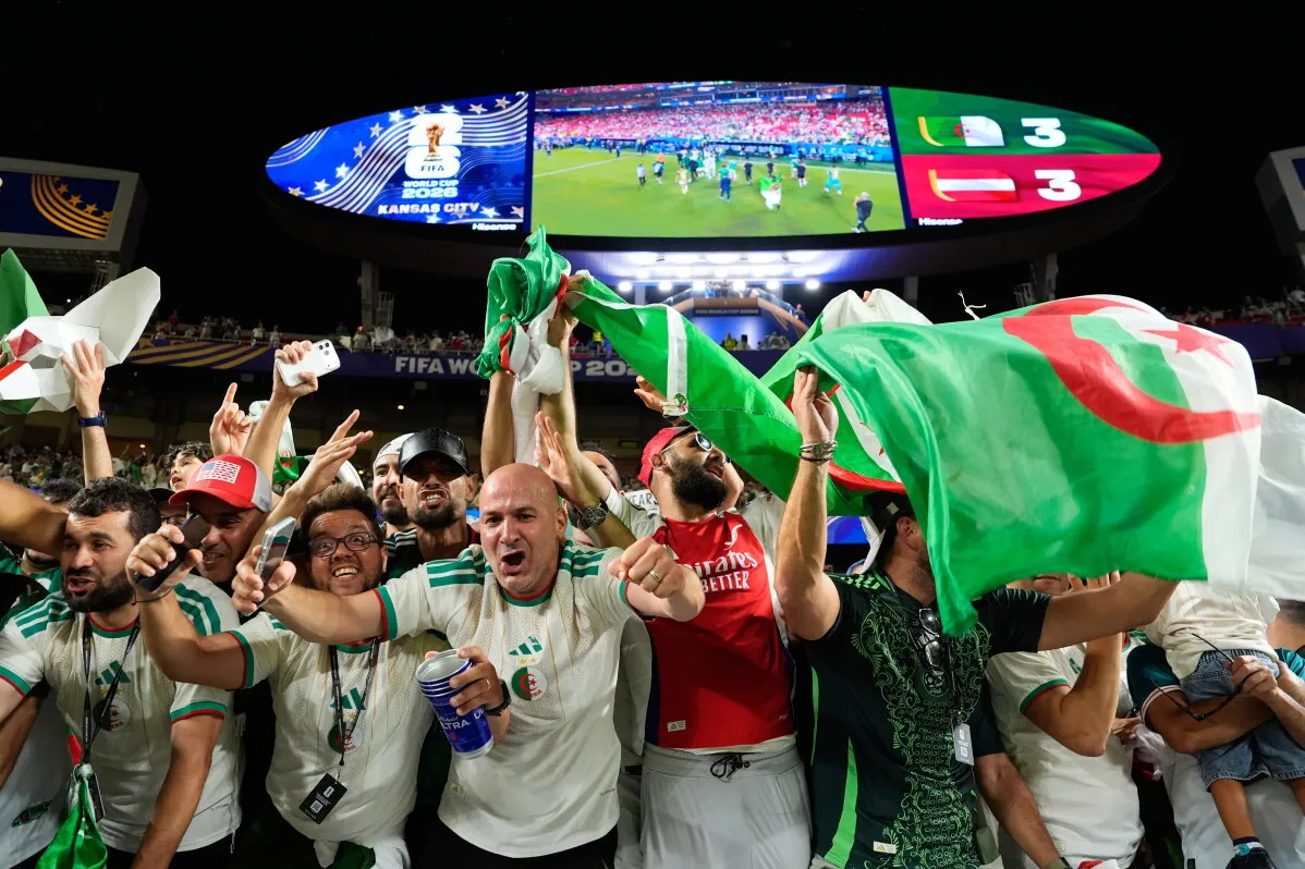 مشجعون جزائريون يحتفلون بحماس في ملعب كرة قدم خلال مباراة كأس العالم 2026، يرفعون العلم الجزائري وسط أجواء حماسية في كانساس سيتي.