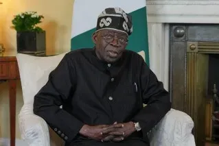 الرئيس النيجيري Bola Tinubu يجلس في غرفة رسمية، مع خلفية تتضمن علم نيجيريا، في سياق محاكمة متهمين بالتخطيط لانقلاب.