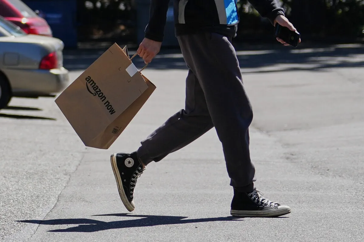 شخص يحمل حقيبة تسوق تحمل شعار "Amazon Now" أثناء سيره في منطقة حضرية، مما يعكس خدمة التوصيل السريع التي تقدمها الشركة.