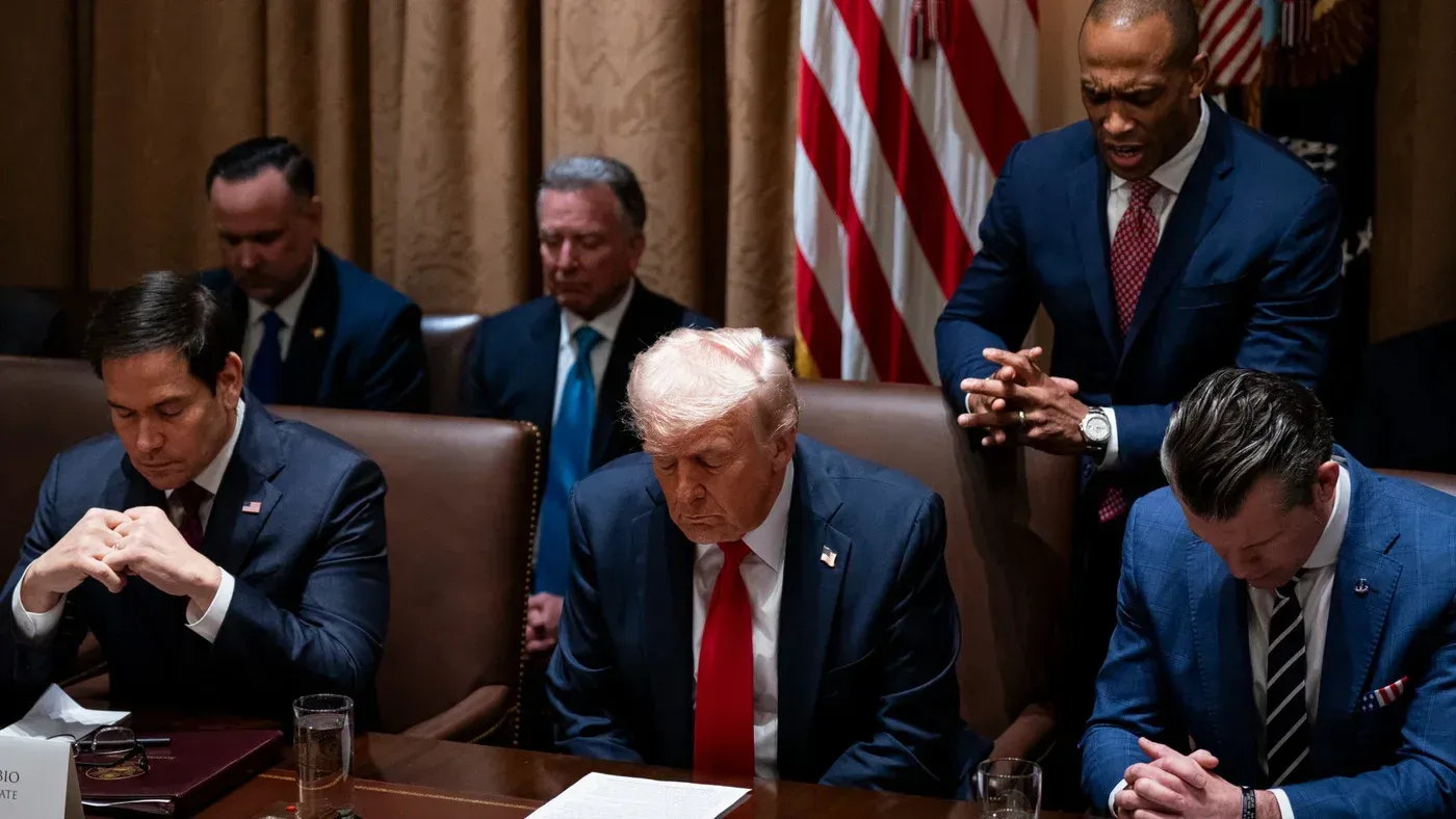 اجتماع سياسي يتضمن شخصيات بارزة، مثل ترامب، وهم يصلون في سياق مناقشة الحرب الإيرانية، مما يعكس تأثير الدين على السياسة الأمريكية.