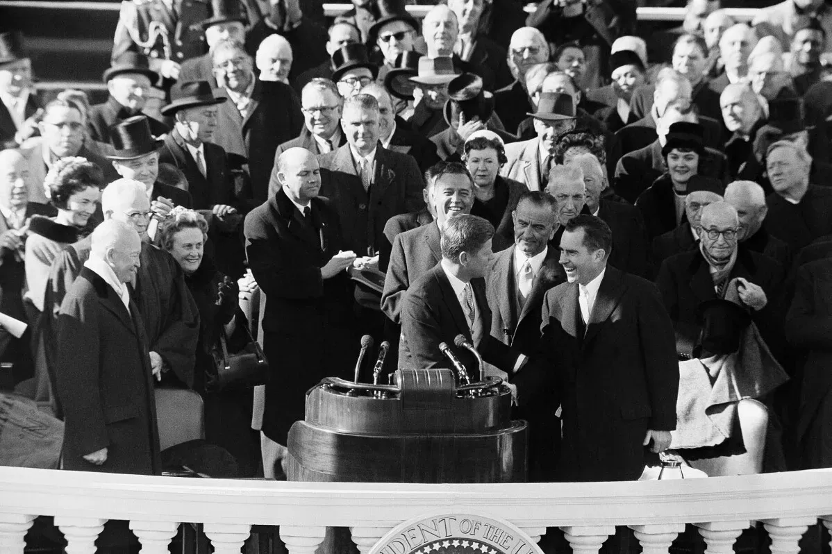 لقاء تاريخي بين جون كينيدي وريتشارد نيكسون خلال حفل تنصيب كينيدي في 1961، مع جمهور كبير خلفهم.