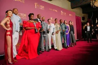 مجموعة من الممثلين الفائزين في حفل جوائز الممثلين، يرتدون ملابس أنيقة، يقفون على السجادة الحمراء مع الجوائز في أيديهم.