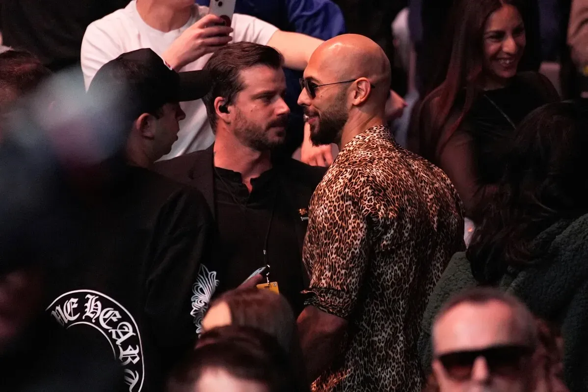 أندرو تيت يتحدث مع شخص آخر في قاعة تي موبايل أرينا خلال حدث UFC 313، وسط حشد من الجمهور.