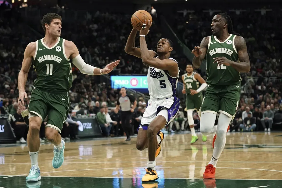 لاعب من فريق ساكرامنتو يسدد الكرة بينما يحاول لاعبان من ميلووكي باكس إيقافه، في مباراة NBA انتهت بفوز باكس 130-115.