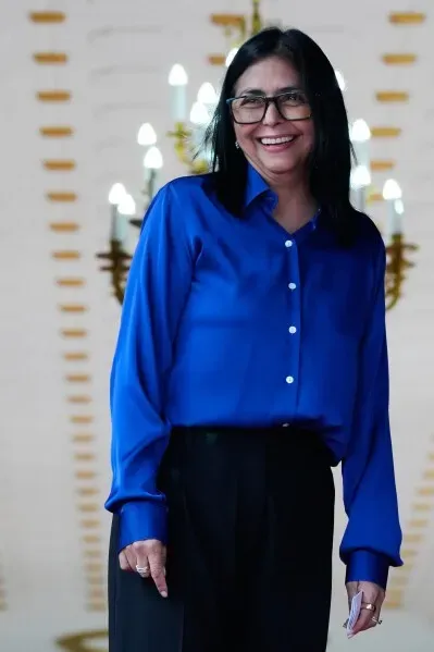 ديليسي رودريغيز، نائبة الرئيس الفنزويلي، مبتسمة في قاعة رسمية، ترتدي قميصًا أزرق وبنطالًا أسود، وسط أجواء سياسية متوترة.