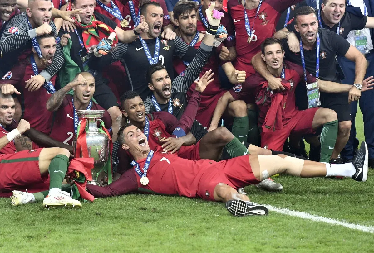 احتفال فريق البرتغال بفوزهم ببطولة يورو 2016، حيث يظهر كريستيانو رونالدو مستلقيًا مبتسمًا مع الكأس، محاطًا بزملائه.