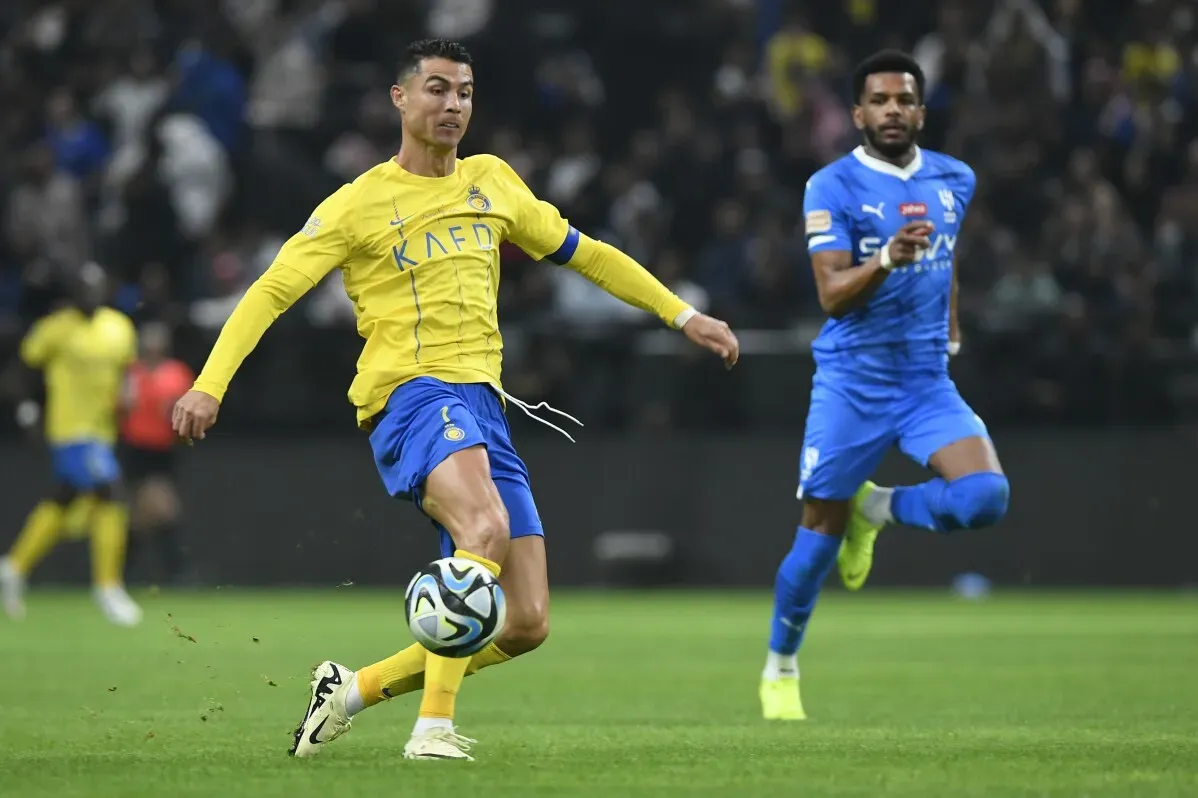 كريستيانو رونالدو يرتدي زي نادي النصر السعودي، يركل الكرة بينما يتابعه لاعب من الفريق المنافس في مباراة كرة قدم.