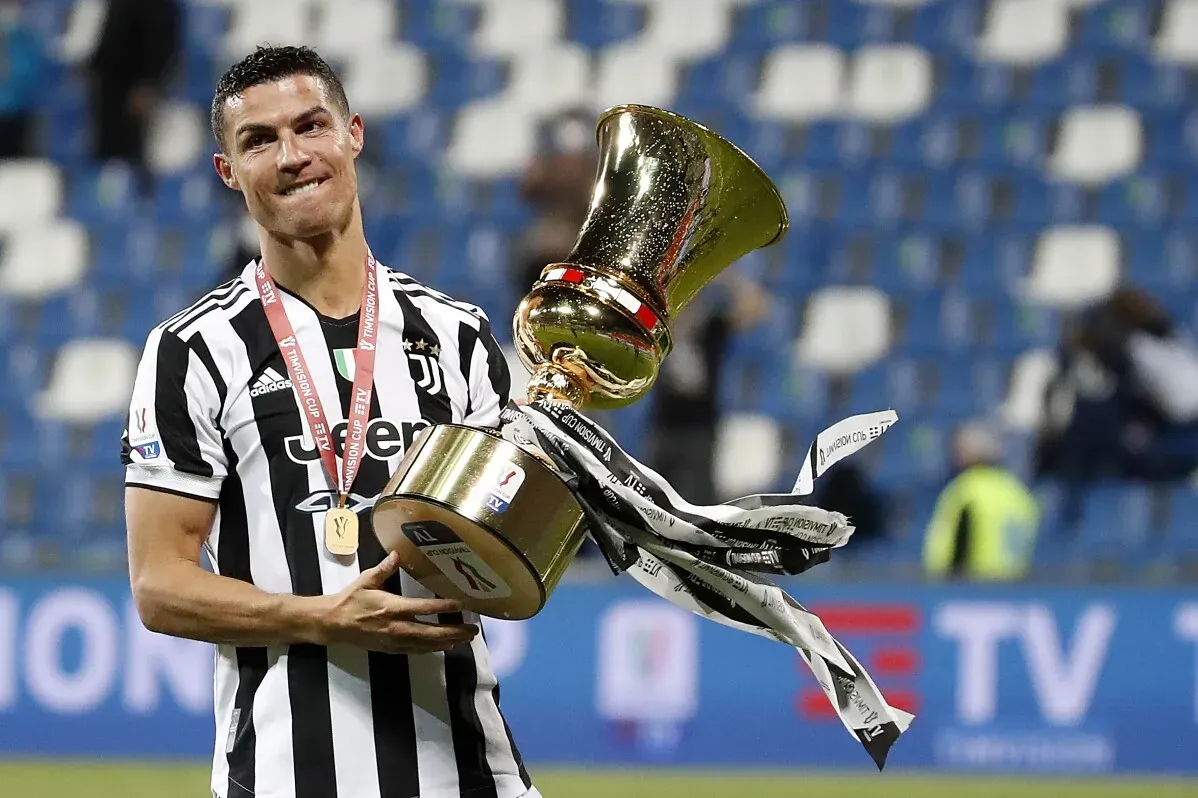رونالدو يحمل كأس البطولة بفخر، مرتديًا قميص يوفنتوس، ويظهر الابتسامة بعد تحقيقه للقب، مما يعكس نجاحه المستمر في مسيرته الرياضية.