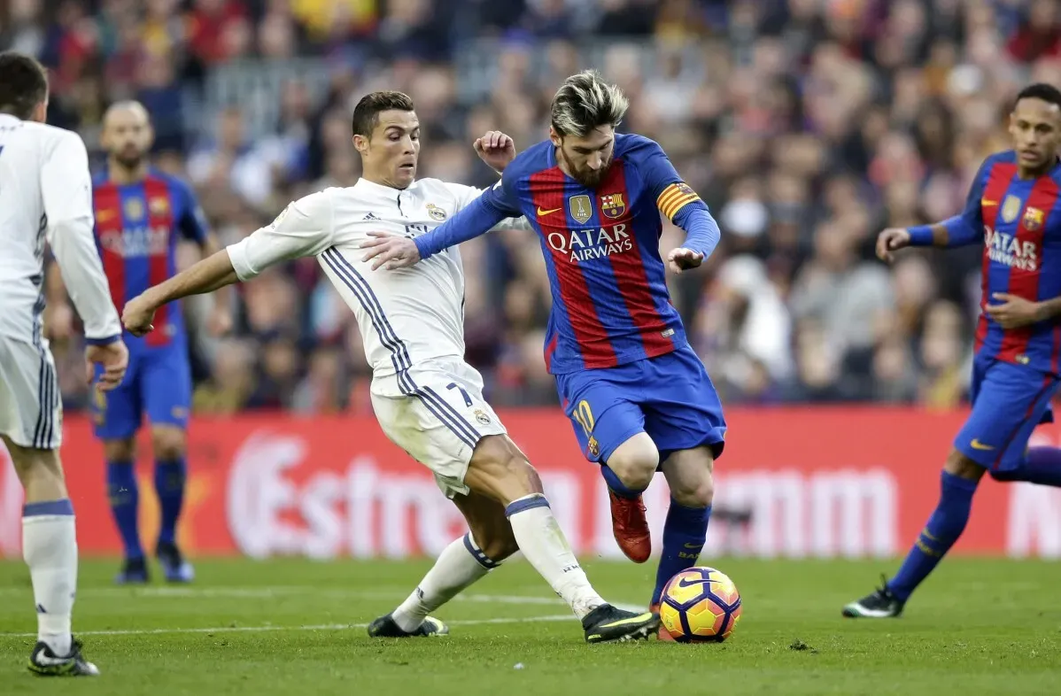 رونالدو يتنافس مع ميسي خلال مباراة كلاسيكو بين ريال مدريد وبرشلونة، مع تواجد لاعبين آخرين في الخلفية.