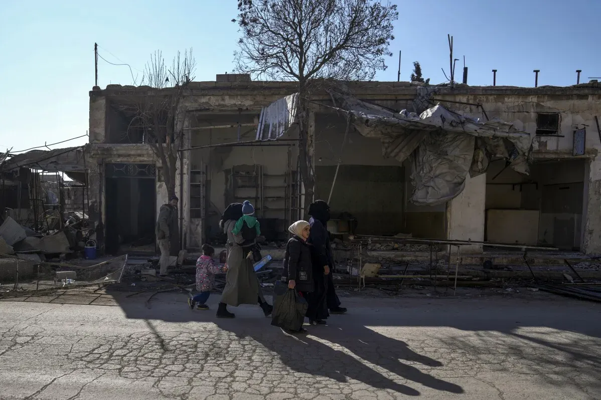 عائلات تسير في شوارع تل رفعت المدمرة، حيث تظهر آثار الحرب والركام حول المباني المتهدمة، مما يعكس واقع العودة الصعب.