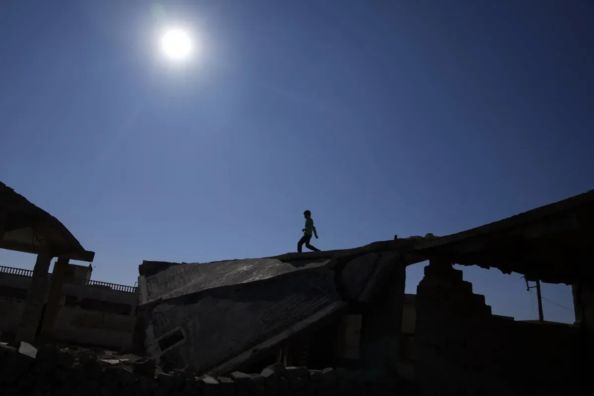طفل يسير فوق أنقاض مبنى مهدوم في تل رفعت، سوريا، تحت شمس ساطعة، مما يعكس آثار الحرب والدمار في المنطقة.