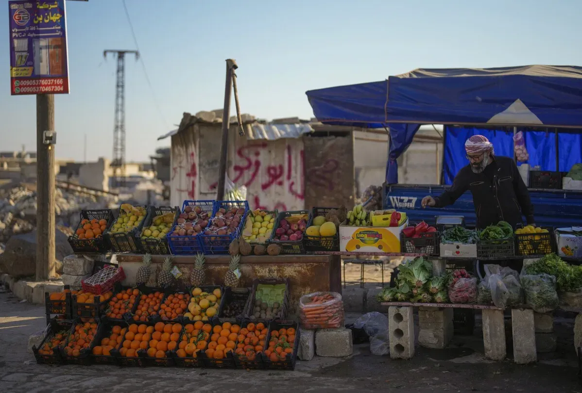 بائع خضار وفواكه في سوق بتل رفعت، سوريا، وسط أنقاض الحرب، يعرض مجموعة متنوعة من المنتجات الطازجة.