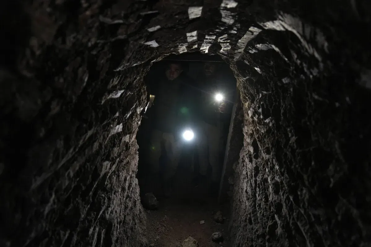 تظهر الصورة نفقًا مظلمًا تحت الأرض في تل رفعت، حيث يحمل الأشخاص مصابيح، مما يعكس آثار الحرب والتحديات التي تواجه العودة.