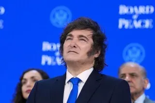 رجل يرتدي بدلة زرقاء يتطلع إلى الأعلى، مع خلفية زرقاء تحمل شعار "مجلس السلام"، في سياق اتفاق تجاري بين الأرجنتين والولايات المتحدة.