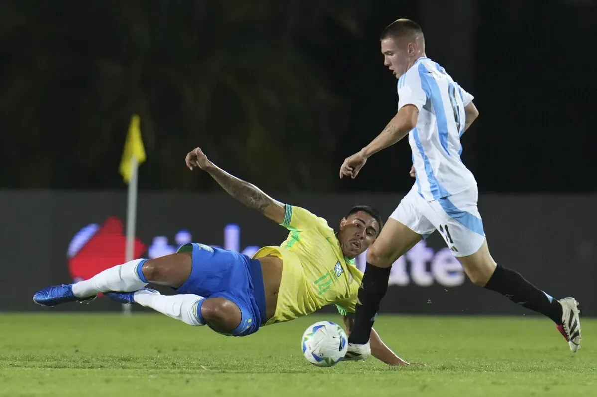 مباراة بين المنتخب الأرجنتيني والبرازيل تحت 20 عام، حيث يسقط لاعب برازيلي على الأرض بينما يحاول الأرجنتيني الاستحواذ على الكرة.