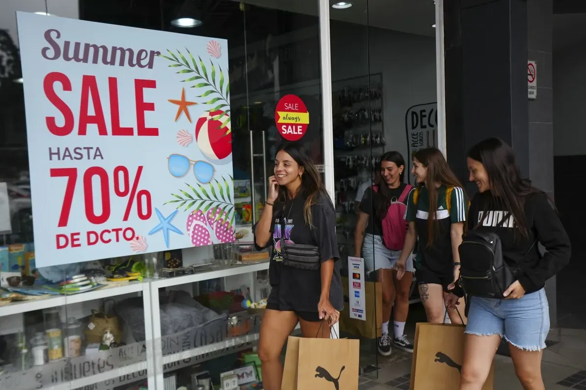 مجموعة من الفتيات يخرجن من متجر يحمل لافتة تخفيضات صيفية تصل إلى 70%، مع أكياس تسوق في أيديهن.