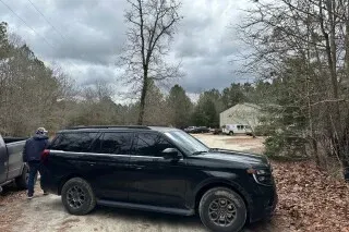 سيارة دفع رباعي سوداء متوقفة في منطقة wooded بالقرب من كاميرون، نورث كارولينا، مع شخص يقف بجوارها، في سياق حادثة تتعلق بأوستن تاكر مارتن.