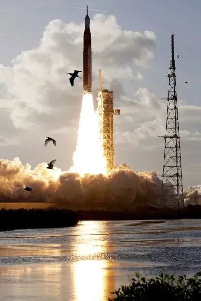 إطلاق صاروخ أرتيميس 2 من كيب كانافيرال، مع سحب الدخان والنار، بينما تحلق الطيور في السماء. المهمة تهدف إلى استكشاف القمر.