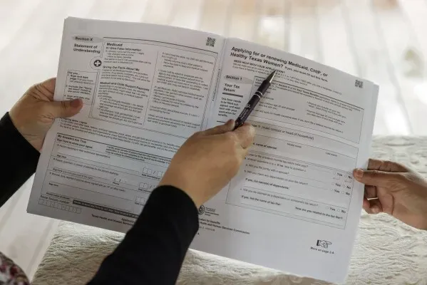 تظهر اليدان وهما تشيران إلى نموذج طلب تجديد برنامج Medicaid، مما يعكس أهمية التمويل والدعم للبرامج الصحية.