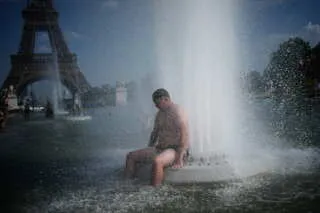 رجل يجلس بجوار نافورة في باريس تحت درجات حرارة مرتفعة، مع برج إيفل في الخلفية، مما يعكس تأثير موجة الحر الأوروبية.