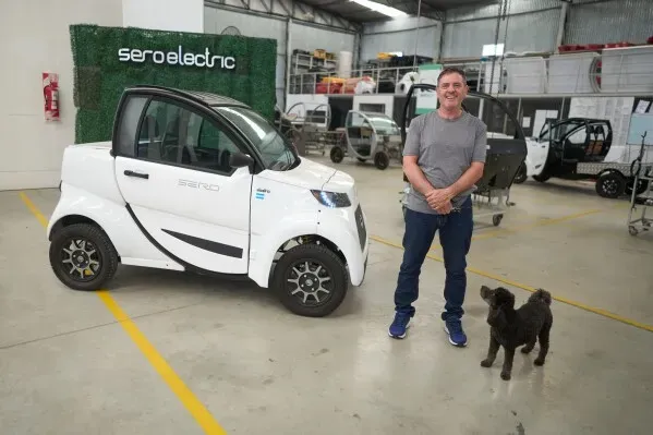 رجل يقف بجانب سيارة كهربائية صغيرة من طراز "سيرو إلكتريك" في ورشة عمل، مع كلب بجانبه، مما يعكس الابتكار في صناعة السيارات في الأرجنتين.