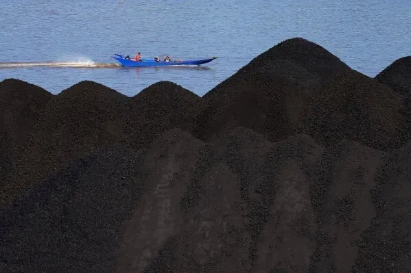 صورة تظهر قاربًا يمر بجوار أكوام من الفحم على ضفاف الماء، مما يعكس الاعتماد المتزايد على الفحم في آسيا لتلبية احتياجات الطاقة.