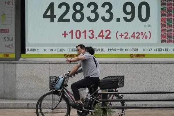 ارتفاع مؤشر نيكاي 225 في طوكيو إلى 42833.90، مع زيادة بنسبة 2.42%، بينما يمر شخصان على دراجة هوائية بجانب الشاشة.